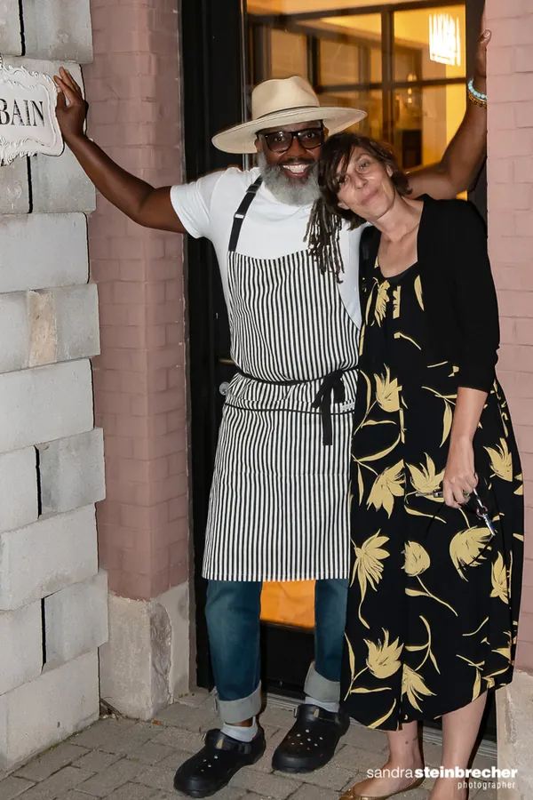 Cliff Rome, in a straw hat and apron, stands with Eileen Rhodes in a doorway.